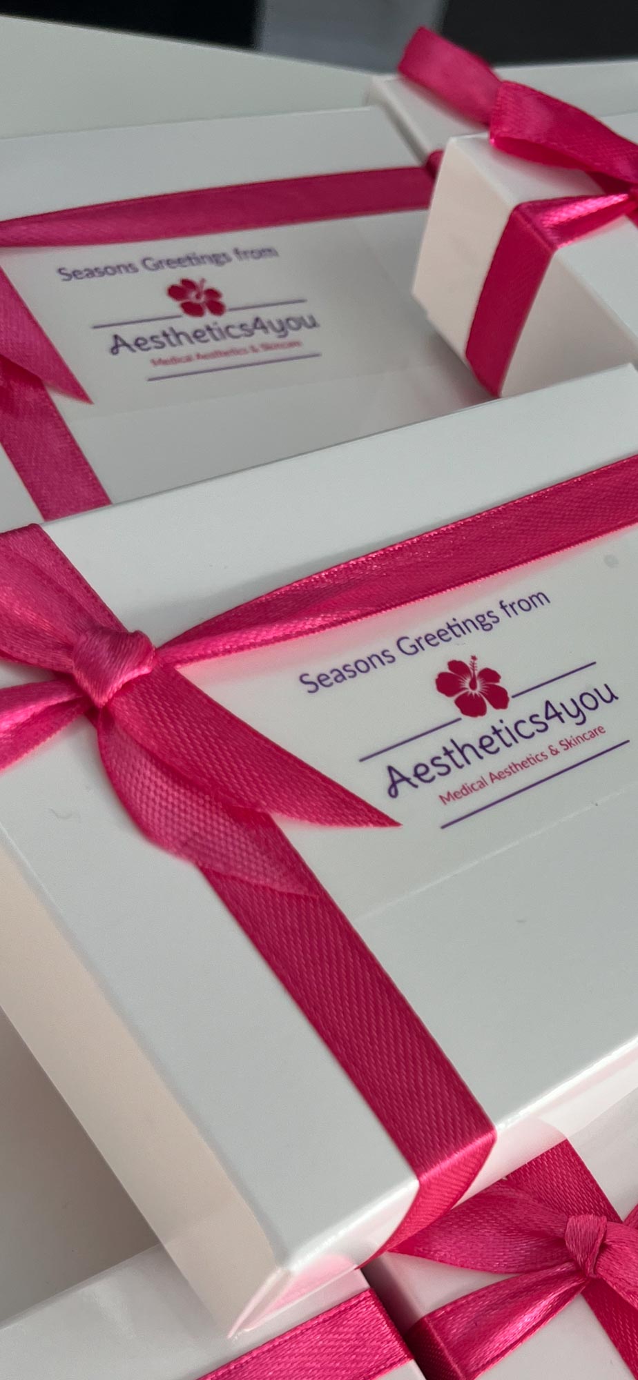White gift boxes wrapped with pink ribbon, featuring "Season's Greetings from Aesthetics4You" on the label.