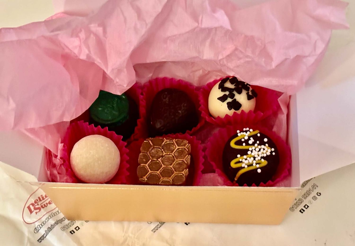 A box of assorted chocolates with different designs in pink paper holders.