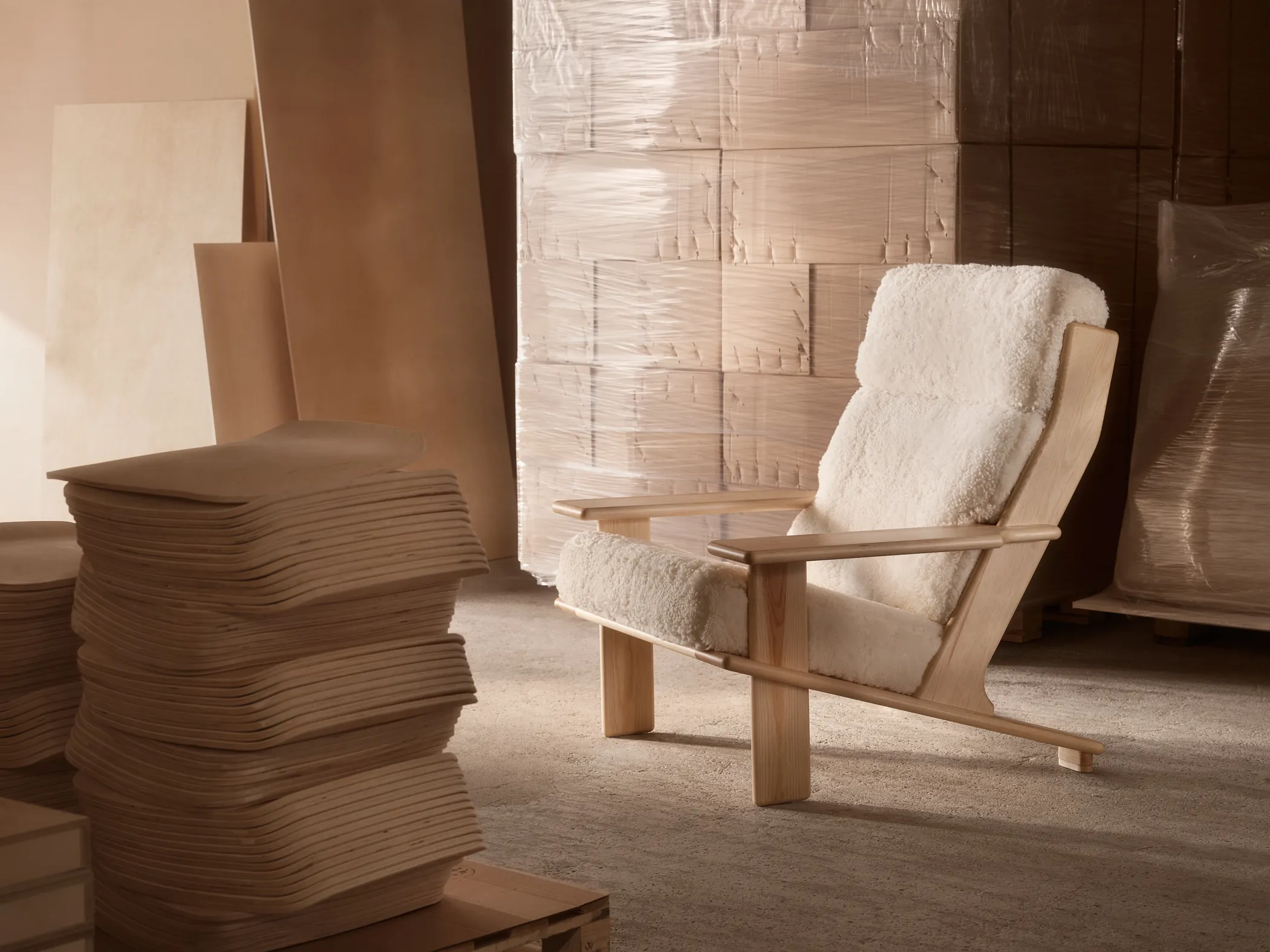 Pehmeä valkoinen nojatuoli vaaleasta puusta teollishuoneessa, vieressä kasa leikattuja puulevyjä.