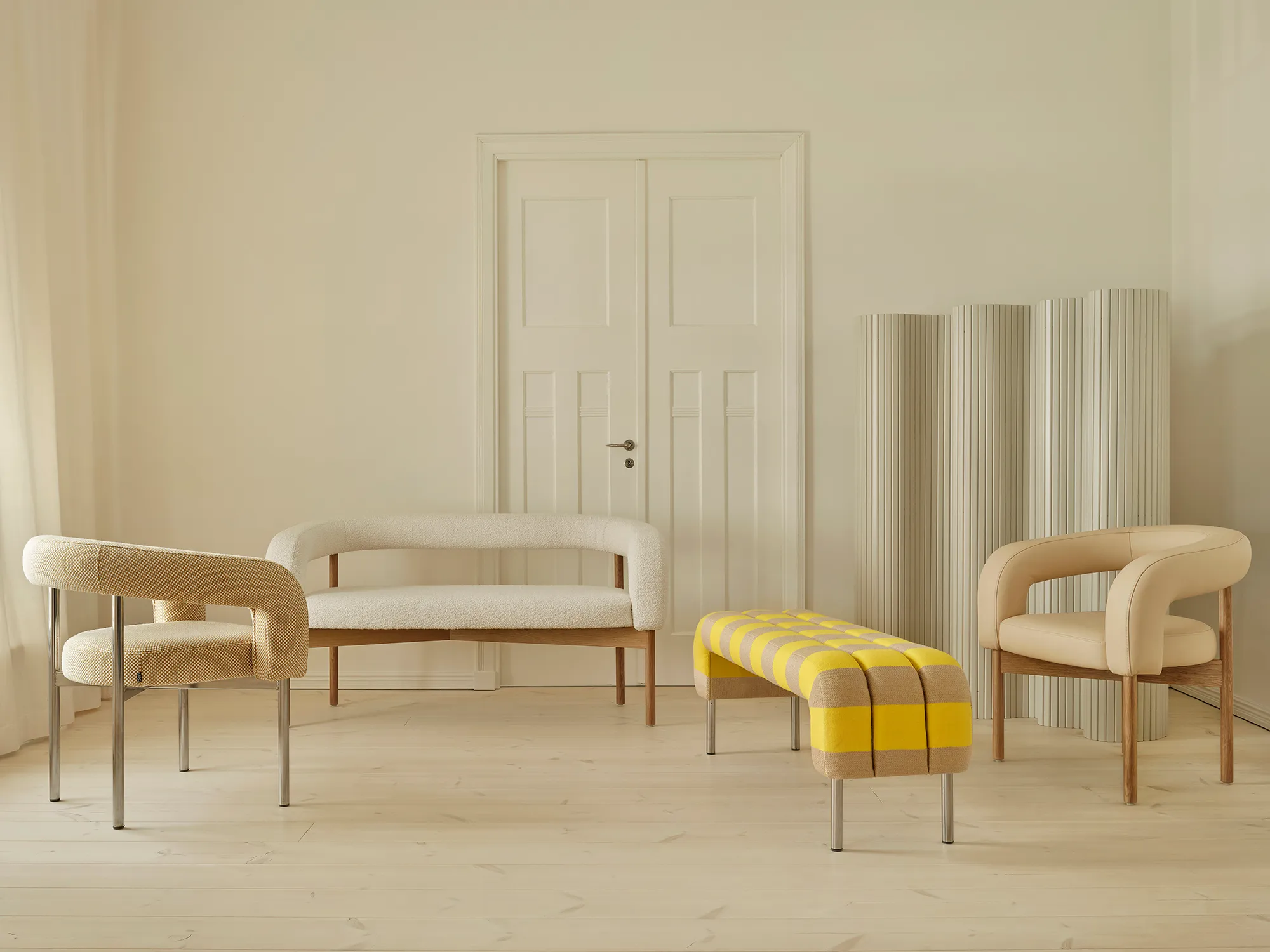 Modern minimalist interior with two beige armchairs, a white cushioned bench, and a yellow and beige checkered ottoman on light wooden floor.