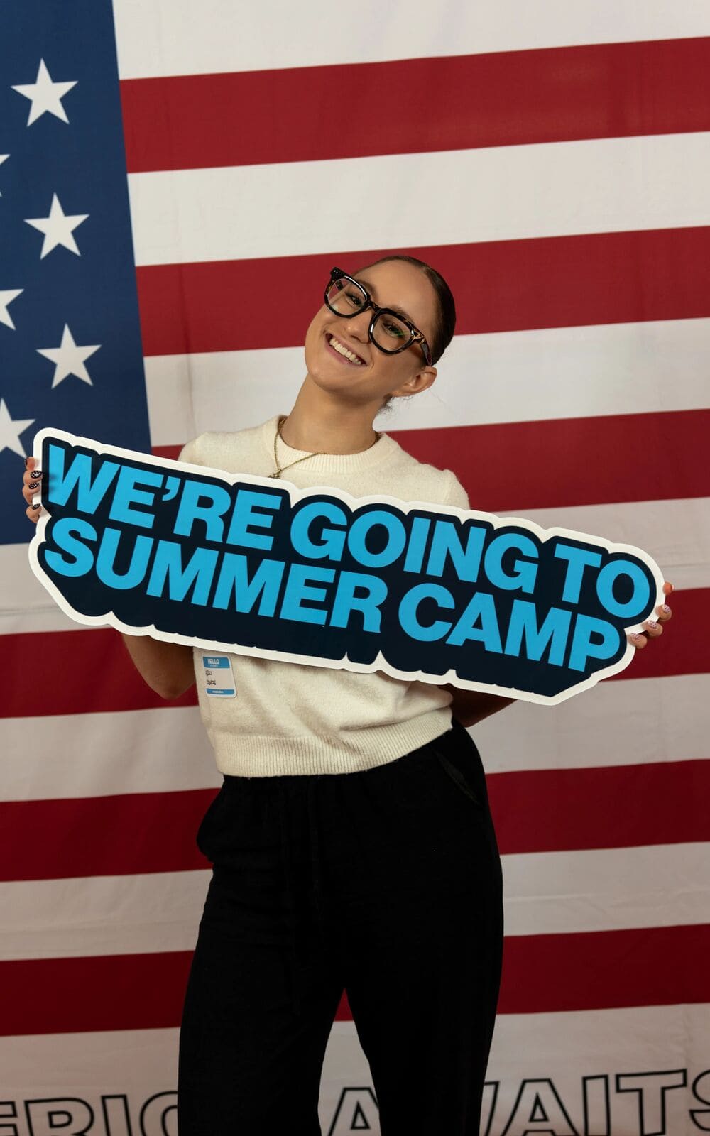 A Hungarian participant holding a sign saying "We're going to summer camp" while standing in front of the US flag