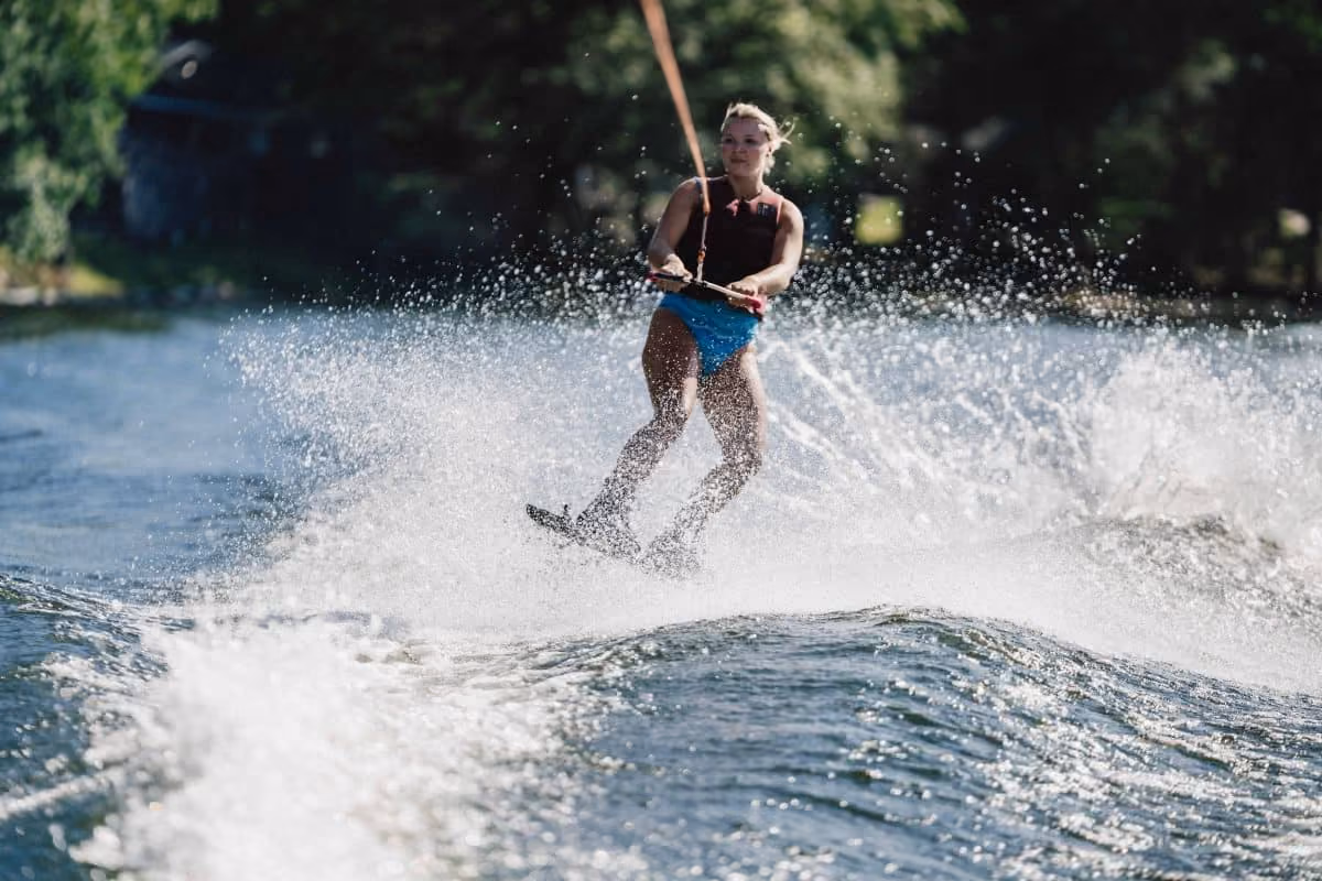 Woman waterskiing on a lake, holding a tow rope handle, with water splashing around her.