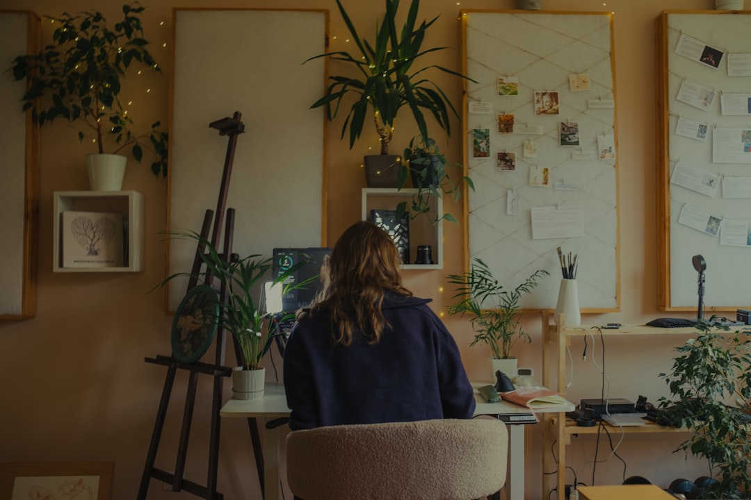Woman working at a desk in a plant-filled studio. for The Small Business Owner's Guide to Using Canva for Professional Brand Design Without Hiring a Designer