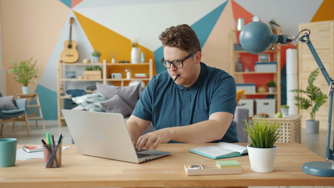 Man working on laptop at a colorful home office desk for "10 Free and Affordable Design Tools That Help Small Businesses Create Professional Branding Without Hiring an Agency"