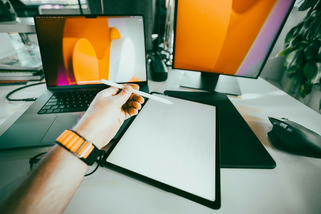 A person's hand on a clipboard next to a computer monitor for The Complete Guide to Choosing Between Figma, Adobe XD, and Sketch for Your Small Business Website Redesign