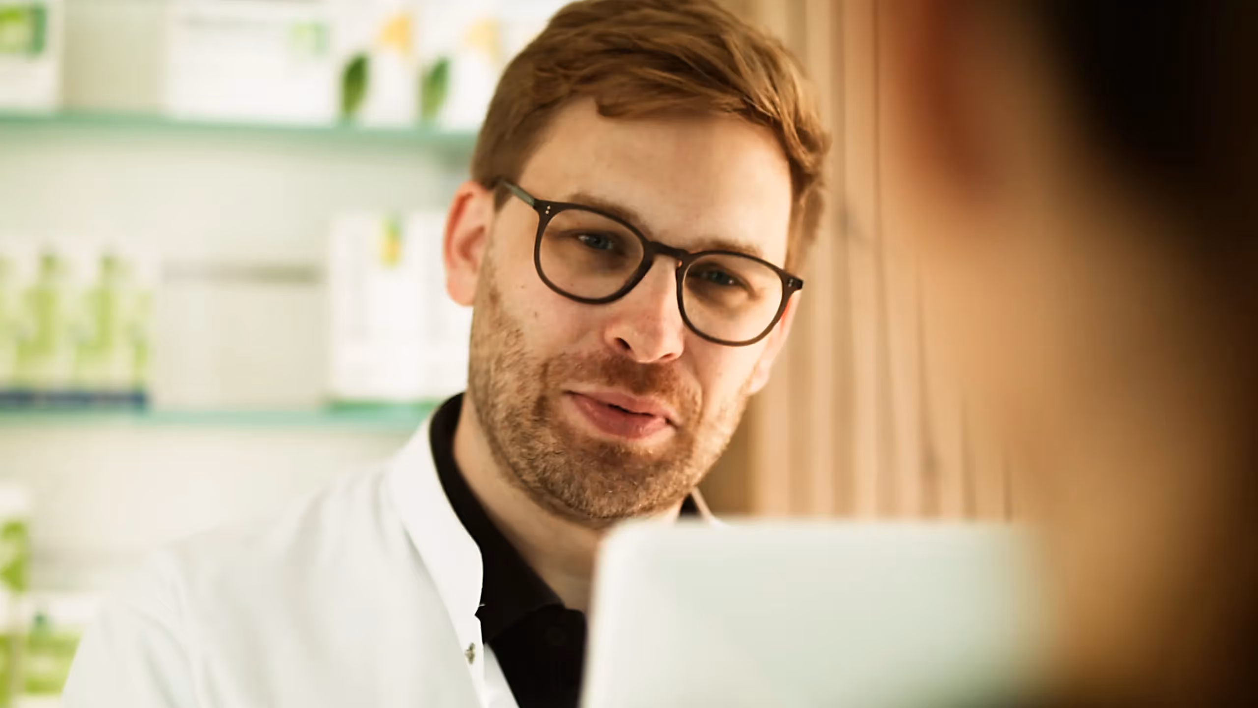 Nahaufnahme eines Arztes im Beratungsgespräch, aufgenommen in heller, moderner Umgebung. Szene aus einem medizinischen Werbefilm oder 2D-Erklärvideo über pharmazeutische Kompetenz, Gesundheit und persönliche Patientenkommunikation.