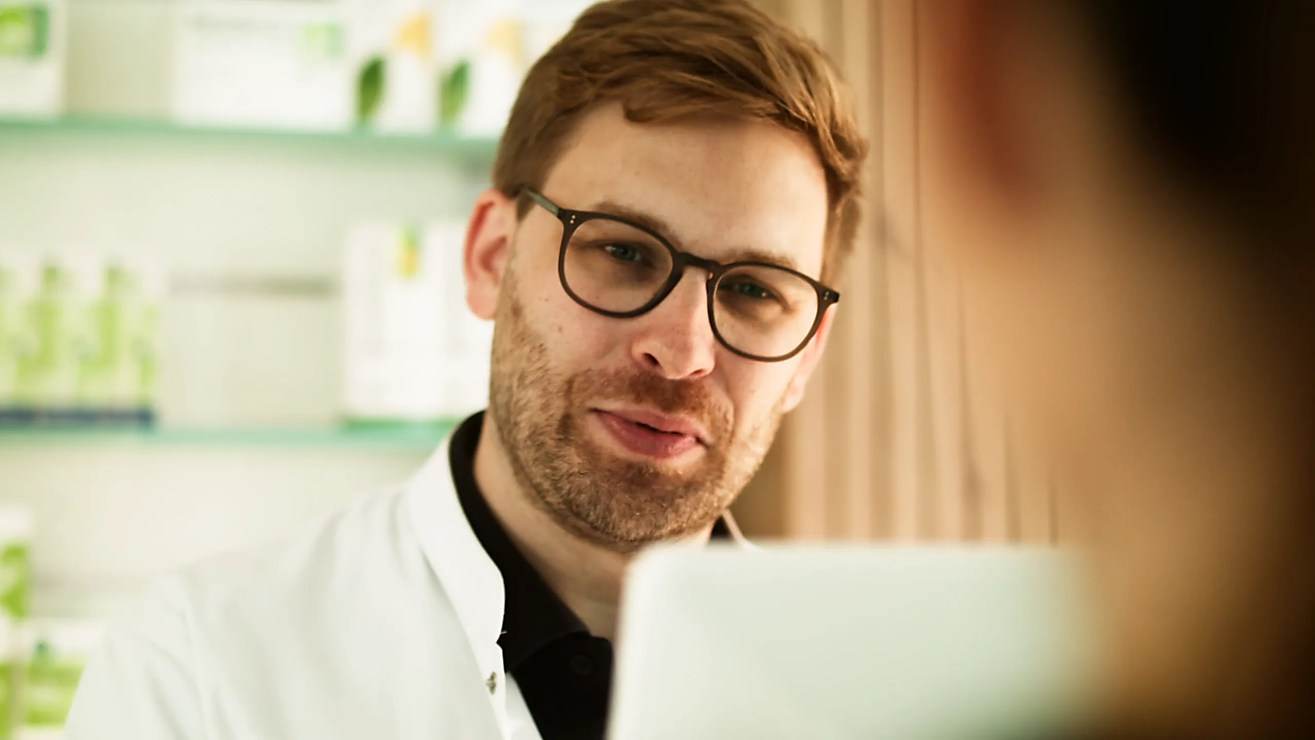 Nahaufnahme eines Arztes im Beratungsgespräch, aufgenommen in heller, moderner Umgebung. Szene aus einem medizinischen Werbefilm oder 2D-Erklärvideo über pharmazeutische Kompetenz, Gesundheit und persönliche Patientenkommunikation.