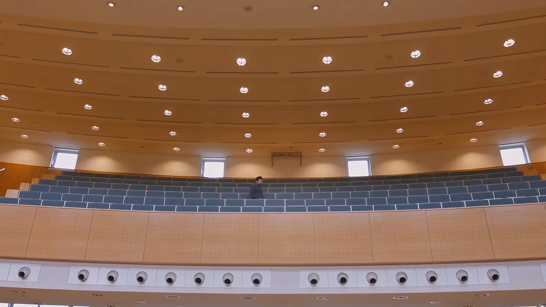 Recruitingfilm Szene: Modernes Hörsaalgebäude mit Holzdecke, blauen Sitzreihen und heller Beleuchtung – filmische Darstellung von Bildung, Campusarchitektur und Lernen in professioneller Filmproduktion und Recruitingfilm.