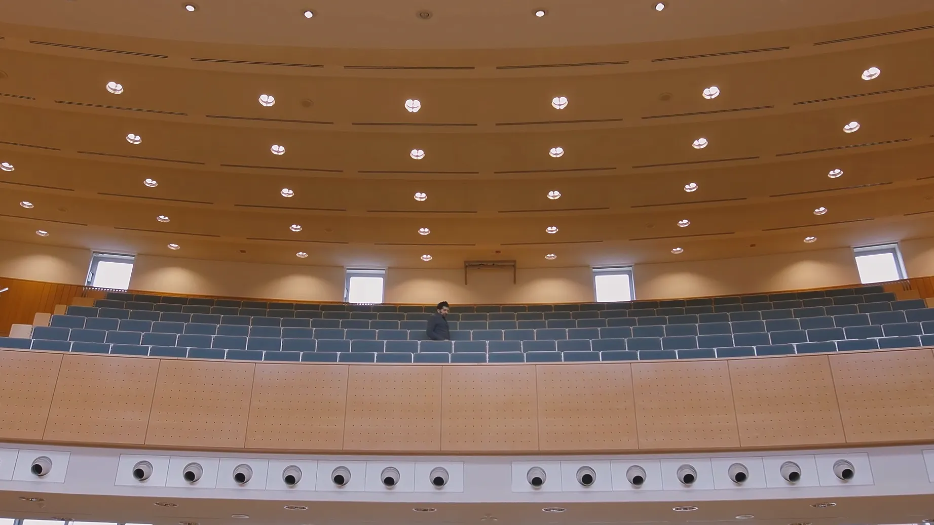 Recruitingfilm Szene: Modernes Hörsaalgebäude mit Holzdecke, blauen Sitzreihen und heller Beleuchtung – filmische Darstellung von Bildung, Campusarchitektur und Lernen in professioneller Filmproduktion und Recruitingfilm.