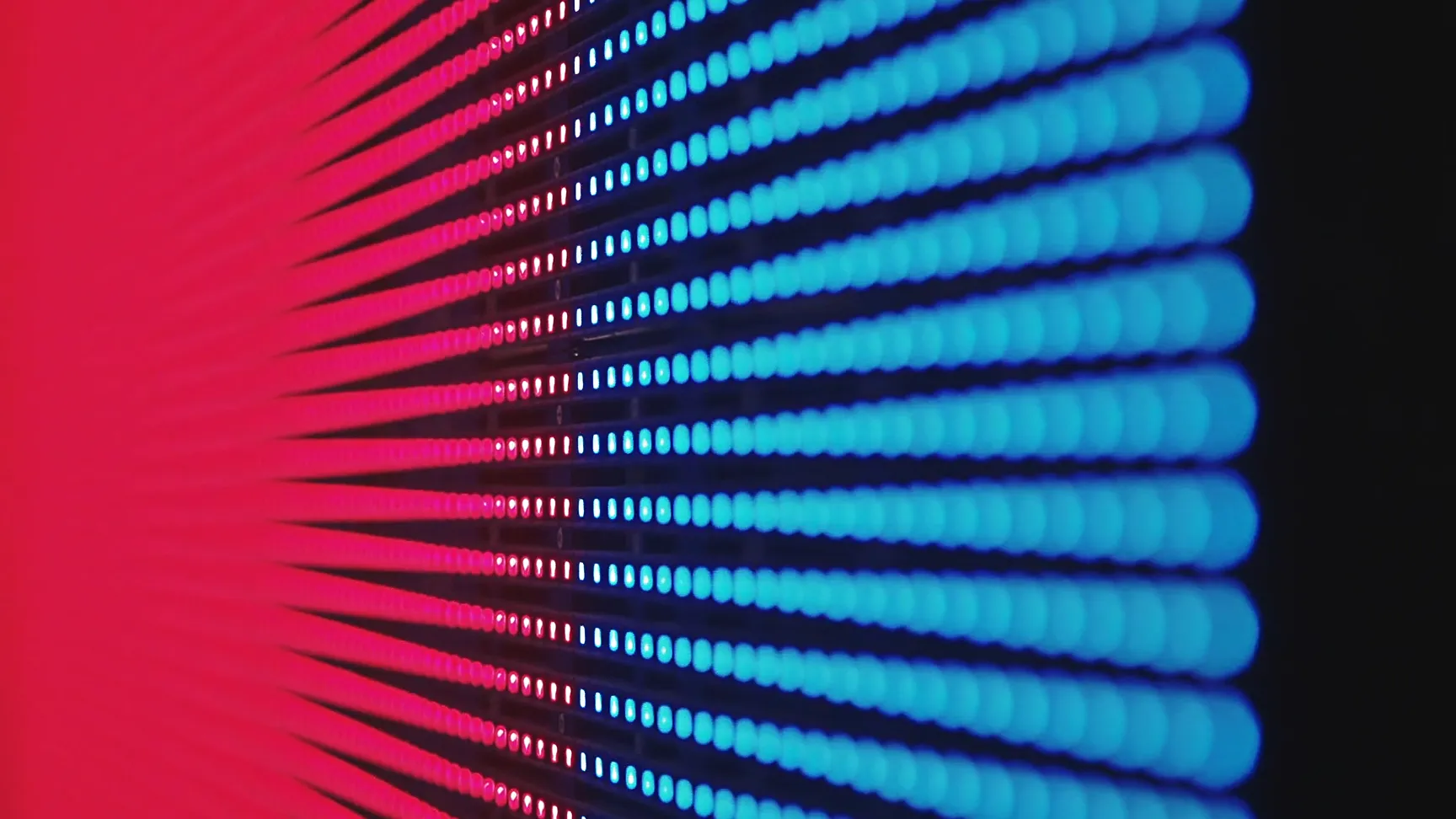 Nahaufnahme einer LED-Wand mit leuchtenden roten und blauen Pixeln, die in horizontalen Reihen angeordnet sind und ein abstraktes Farbspiel erzeugen.