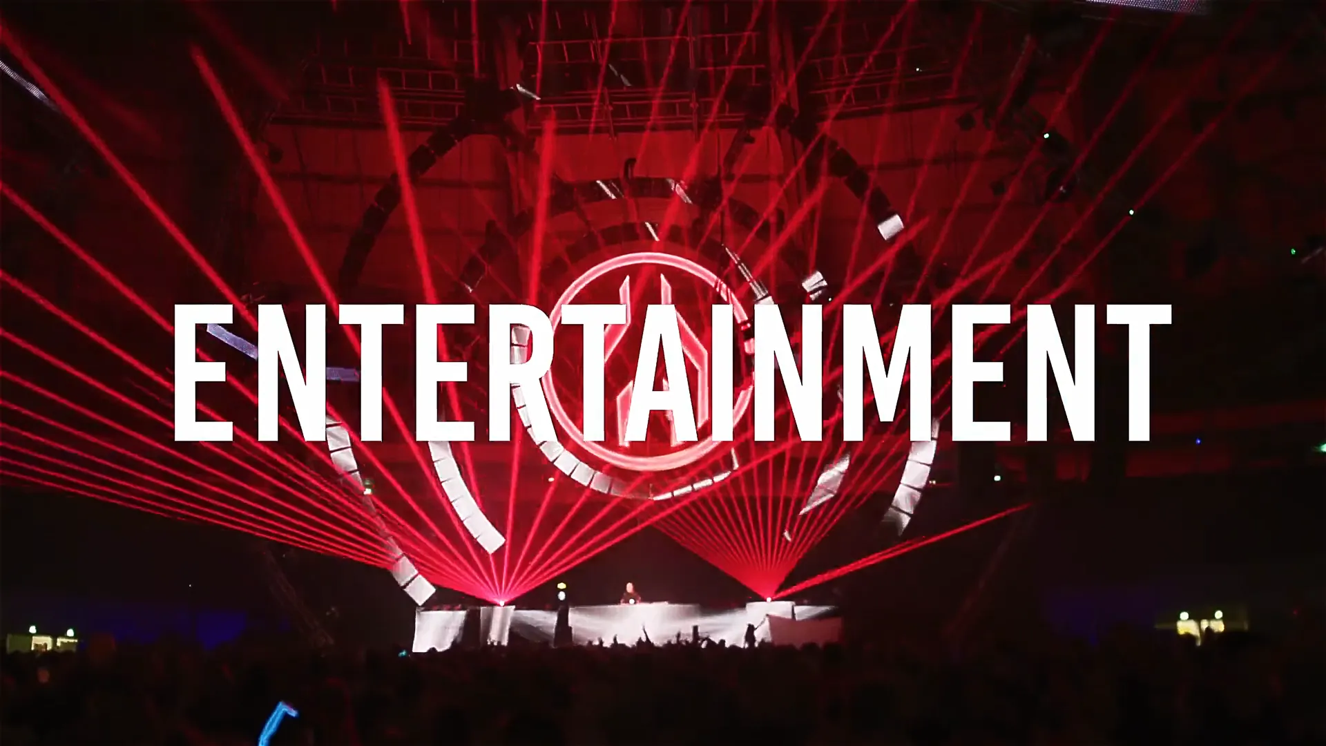 Bühne mit rotem Lasershow-Licht und großem Kreis-Symbol im Hintergrund. Auf der Bühne ein DJ-Pult, davor das Publikum. Groß eingeblendet steht das Wort ENTERTAINMENT in weißer Schrift.