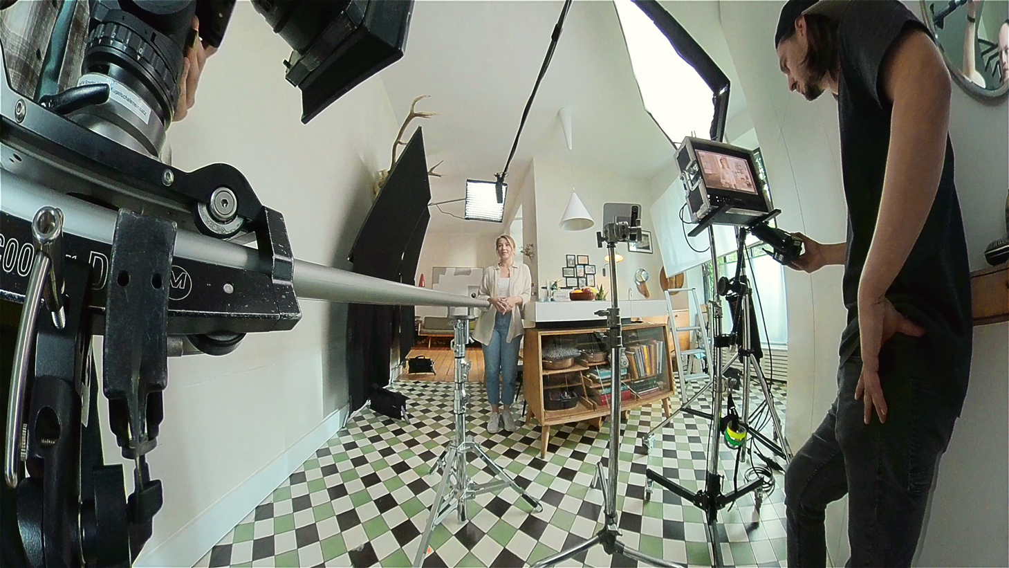 Behind the scenes of a video shoot in a bright kitchen setting – camera crew, lights, and monitor set up around a female presenter