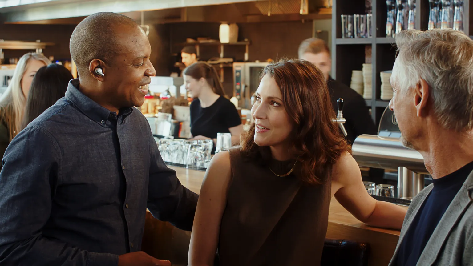 Drei Personen im Gespräch, einer trägt Sennheiser True Wireless Earbuds, Szene im Lifestyle-Werbefilm.