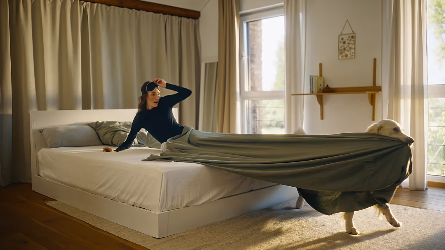 Filmproduktion und Werbefilm-Szene mit spielerischer Produktvideo-Inszenierung: Frau wacht auf, während ein Hund die Bettdecke wegzieht – emotionale Lifestyle-Visualisierung mit Fokus auf Morgenroutine, Alltag und Markenstorytelling.