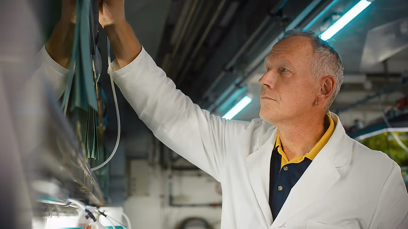 Forscher im weißen Laborkittel bedient technische Anlage mit grüner Beleuchtung, industrielle Laborumgebung, Realfilm, detailreiche Aufnahme.