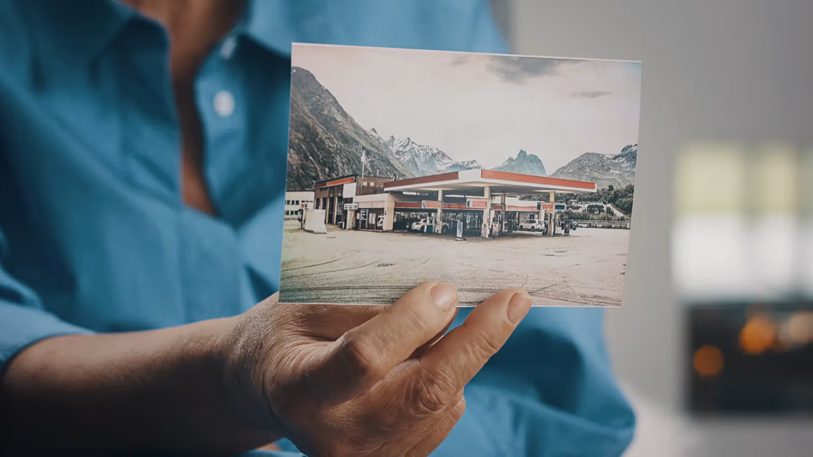 Frau hält ein Foto einer Tankstelle in den Alpen, Symbol für Vergangenheit und Entwicklung von VW.