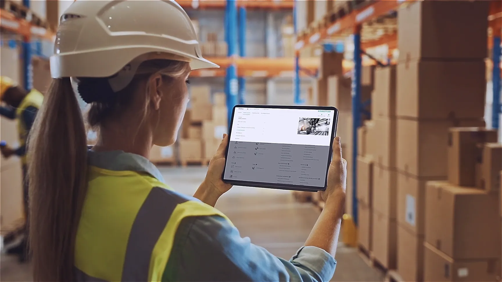 Mitarbeiterin mit Helm nutzt Tablet zur digitalen Lagerverwaltung – Schaeffler setzt auf smarte Intralogistik.