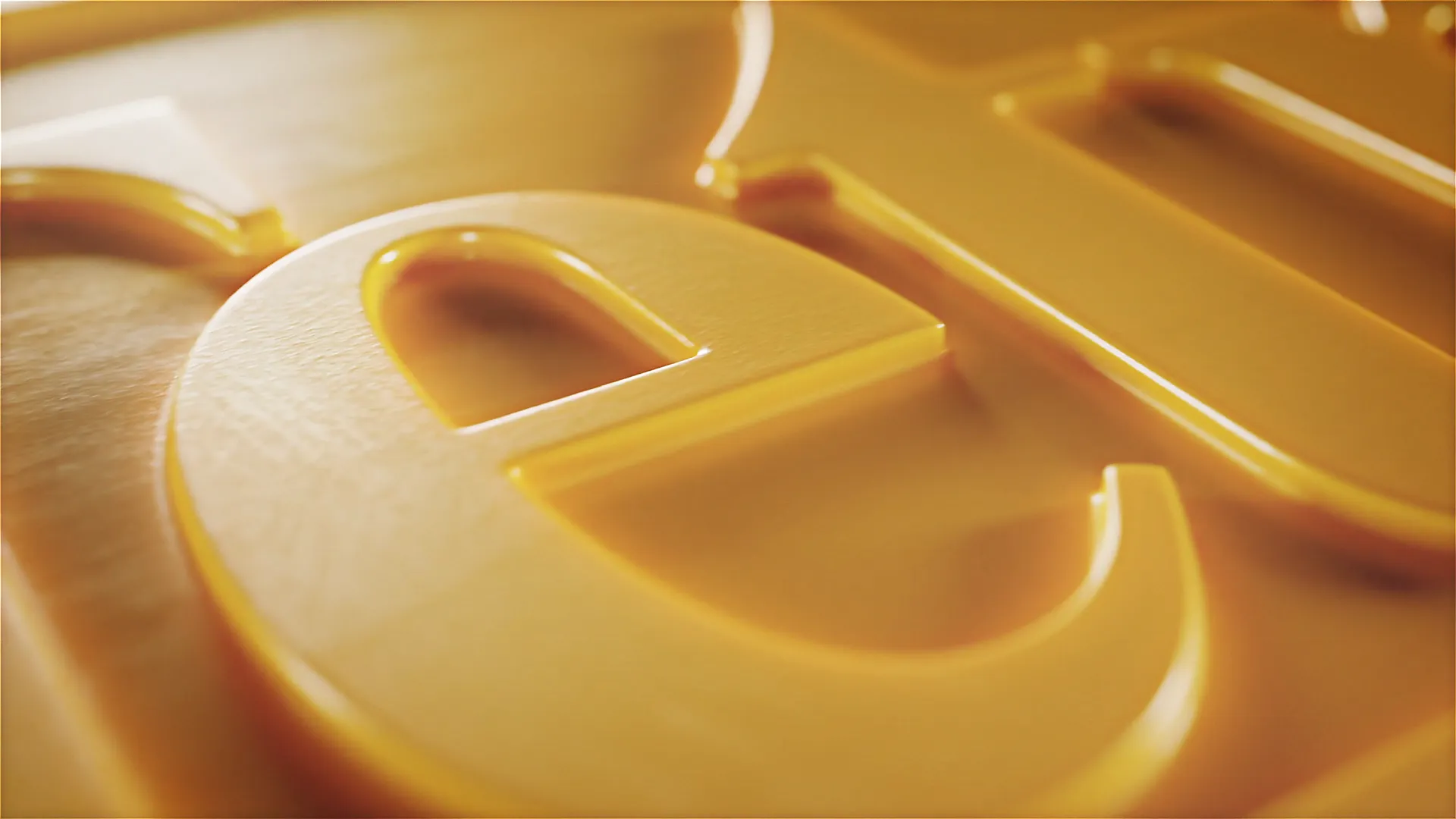 Makroaufnahme einer goldgelben 3D-Prägung: glänzender Buchstabe „e“ aus dem Logo von Tetra, detailreich beleuchtet mit weichen Lichtreflexen – moderne Produktanimation.