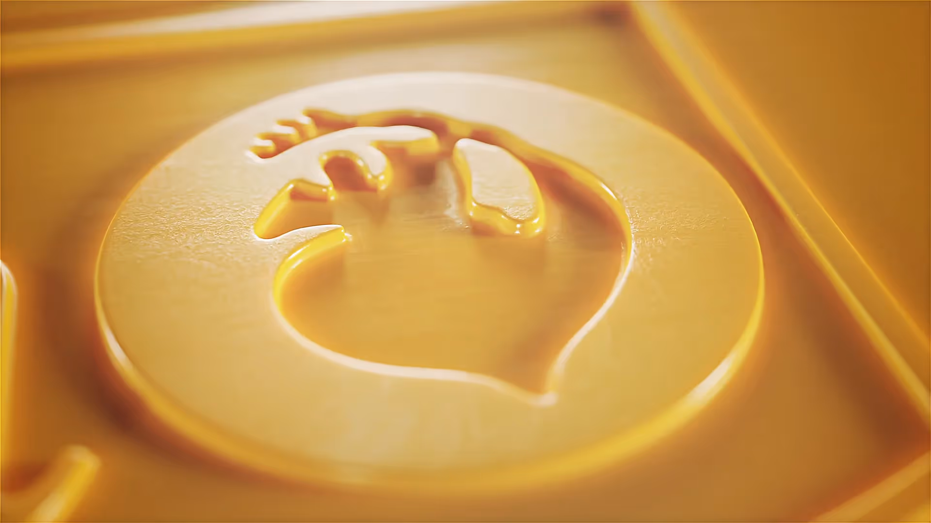 Detailaufnahme einer goldgelben 3D-Prägung mit Fischsymbol im Relief, plastisch hervorgehoben durch weiche Lichteffekte – hochwertige Markeninszenierung.