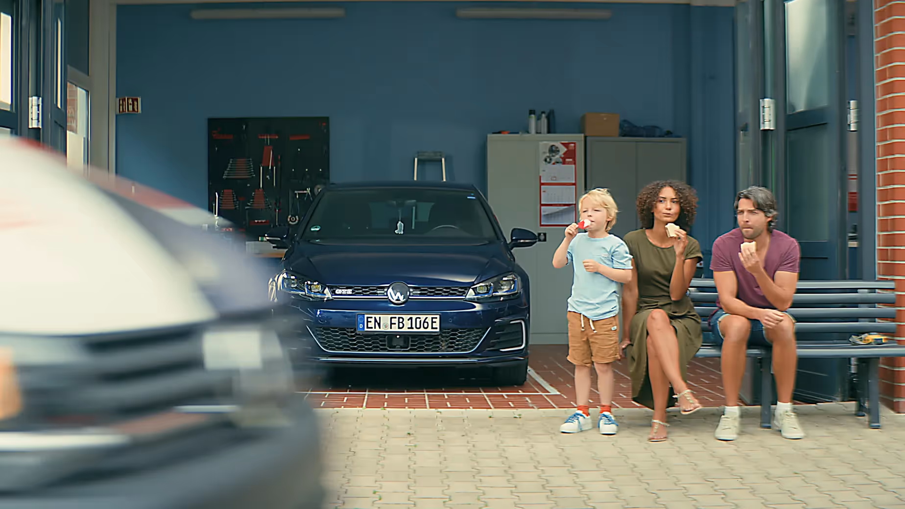 Familie mit Kind sitzt vor Werkstatt isst Eis Auto im Hintergrund FEBI Werbefilm.