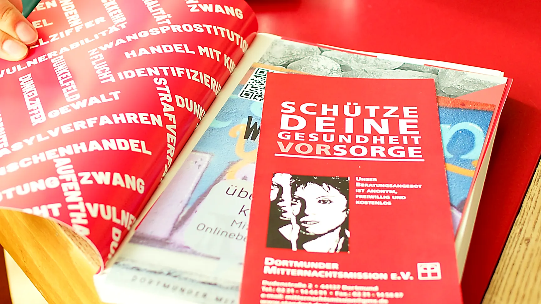 Imagefilm Szene: Ein roter Flyer mit der Aufschrift „Schütze deine Gesundheit Vorsorge“ liegt neben Informationsmaterial – visuelle Darstellung von Bildung, Aufklärung und Gesundheitsbewusstsein im Imagefilm.