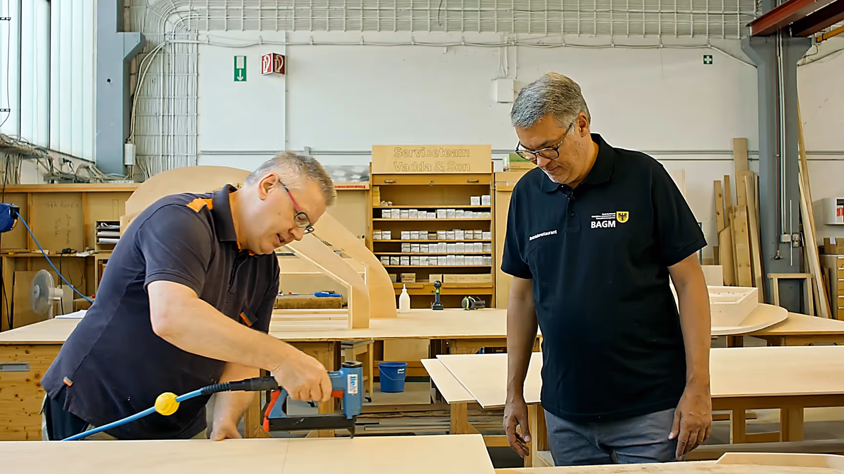 Imagefilm Szene: Zwei Handwerker arbeiten konzentriert in einer Werkstatt mit Holzplatten und Werkzeugen – authentische Darstellung von Bildung, Handwerk und Ausbildung im Imagefilm von CHEESE Productions.
