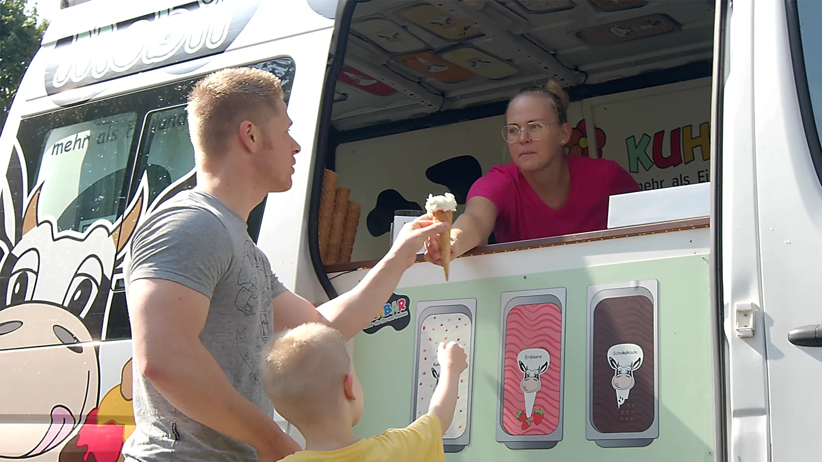Imagefilm Szene: Ein Mann und ein Kind erhalten eine Eiswaffel von einer Verkäuferin im Eiswagen – emotionale Darstellung für Bildung, Gemeinschaft und Wertevermittlung im Imagefilm von CHEESE Productions.