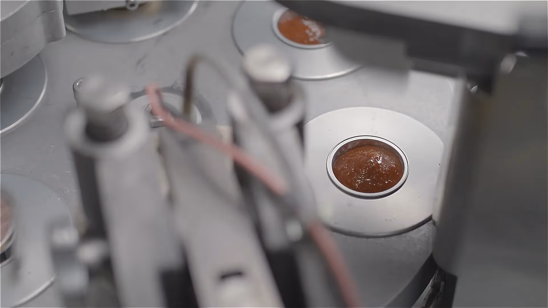 Produktionsmaschine: Nahaufnahme einer runden Futterdose mit brauner Masse, Teil der Abfüllanlage – moderne industrielle Fertigung.