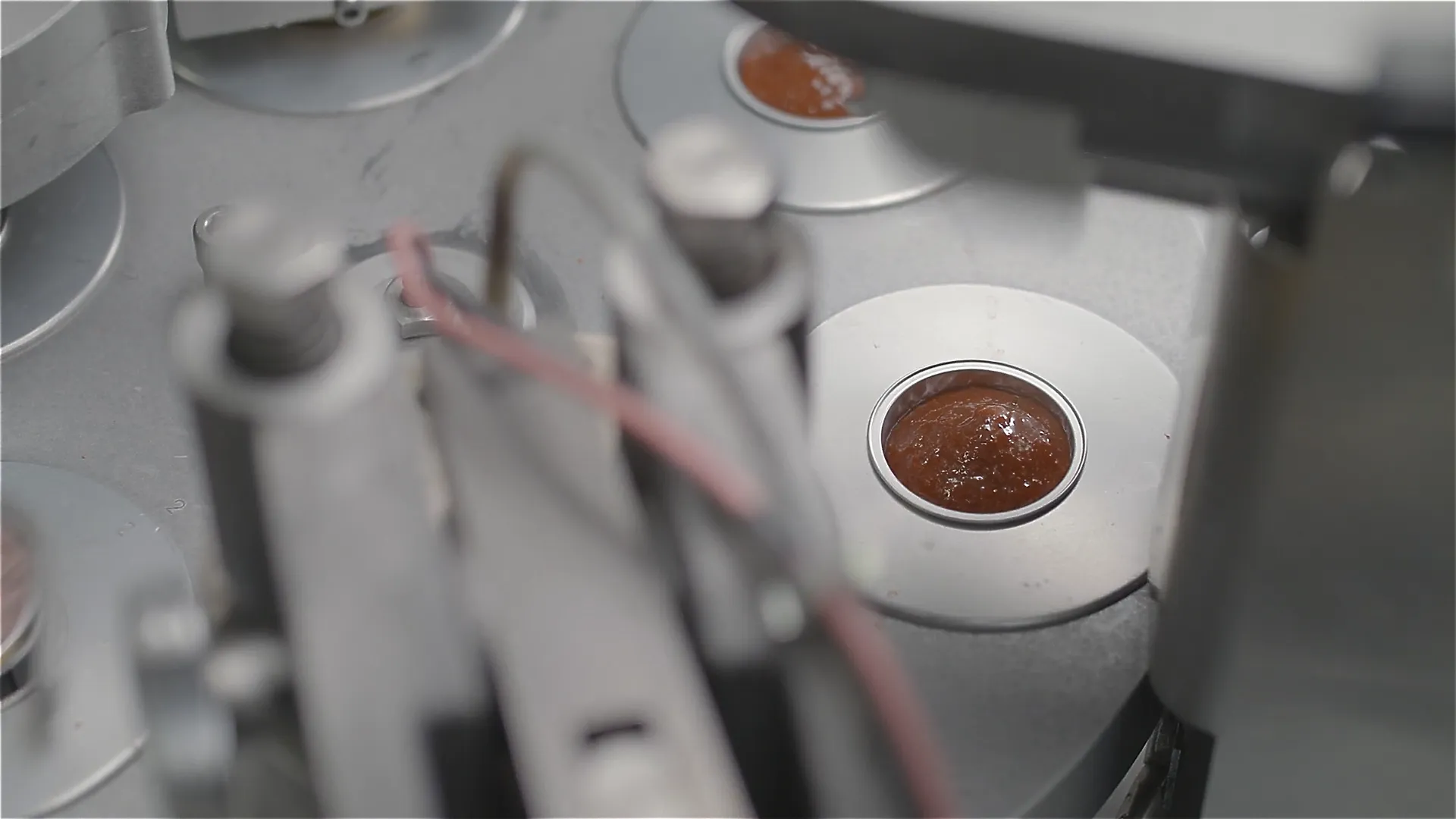 Produktionsmaschine: Nahaufnahme einer runden Futterdose mit brauner Masse, Teil der Abfüllanlage – moderne industrielle Fertigung.