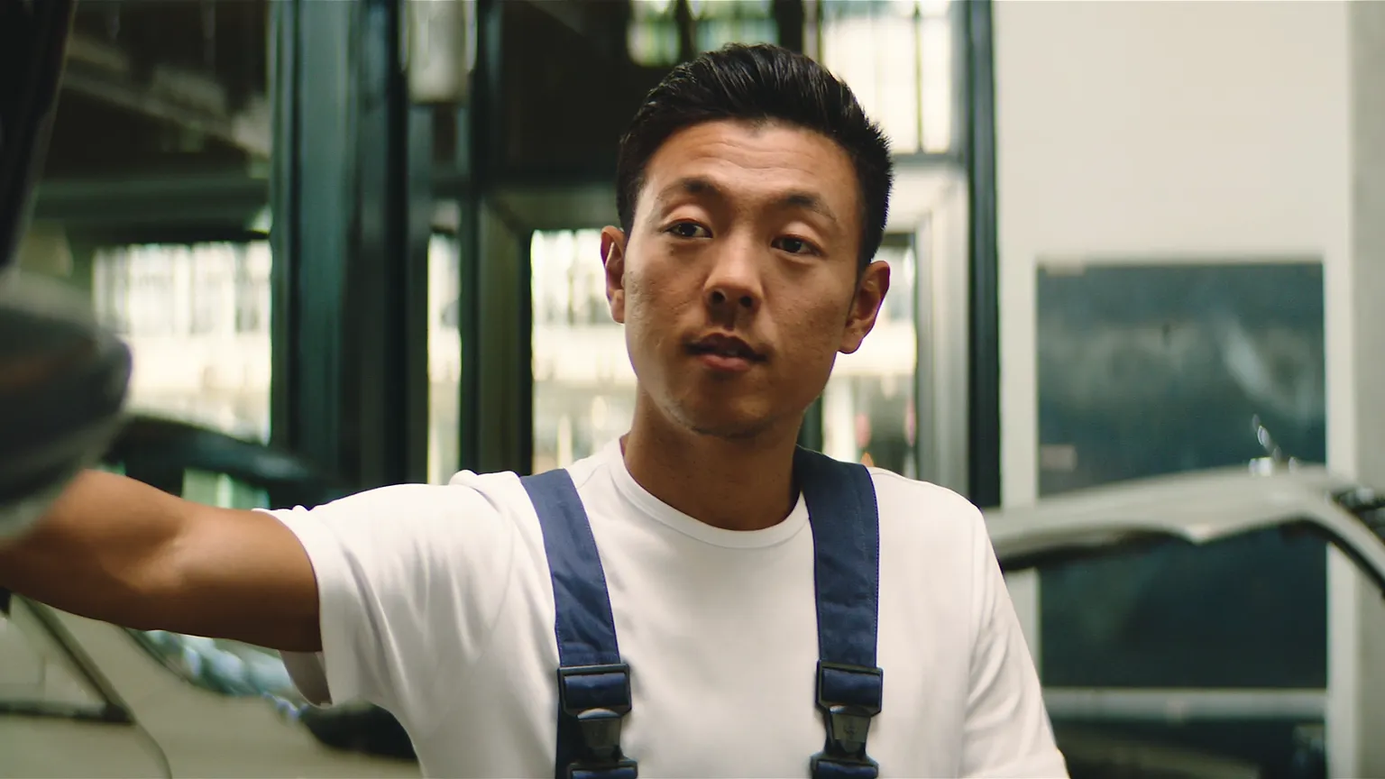 Automechaniker in blauer Arbeitskleidung erklärt jungen Auszubildenden den Beruf in einer Werkstatt.