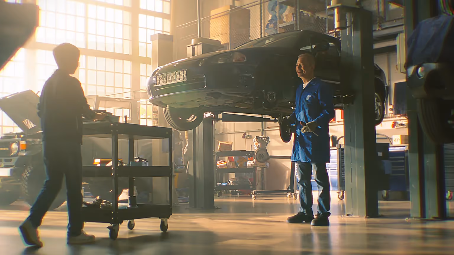 Zwei Mechaniker arbeiten in einer hellen Autowerkstatt mit Fahrzeug auf Hebebühne.