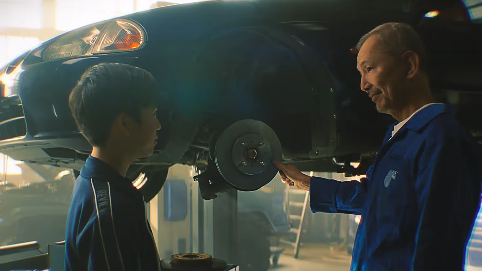 Vater zeigt seinem Sohn in der Werkstatt eine Bremsscheibe an einem Auto.