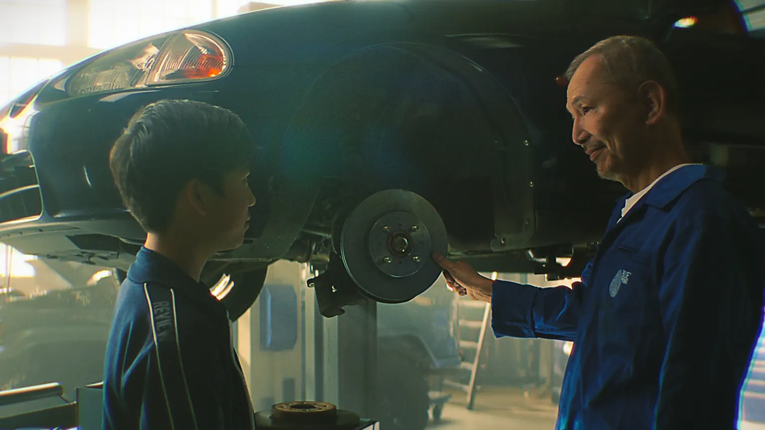 Vater zeigt seinem Sohn in der Werkstatt eine Bremsscheibe an einem Auto.