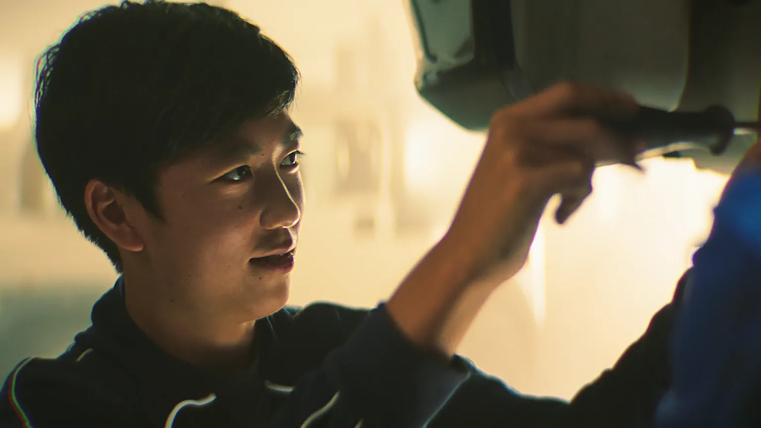 Junge Azubi schraubt konzentriert an einem Auto in einer Werkstatt.