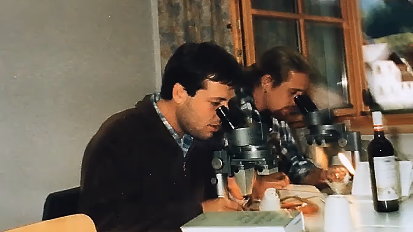 Zwei Wissenschaftler sitzen an Mikroskopen und analysieren Proben – eine historische Aufnahme aus den frühen Forschungstagen.