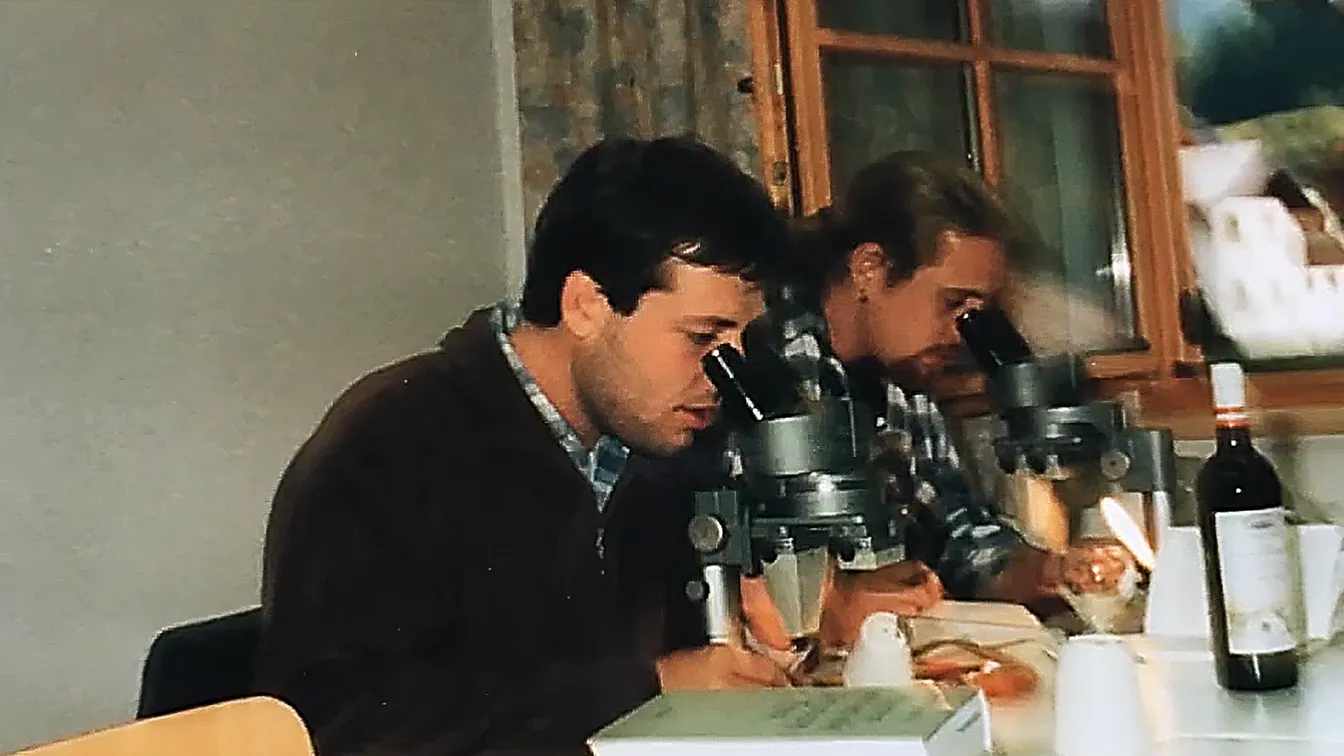 Zwei Wissenschaftler sitzen an Mikroskopen und analysieren Proben – eine historische Aufnahme aus den frühen Forschungstagen.