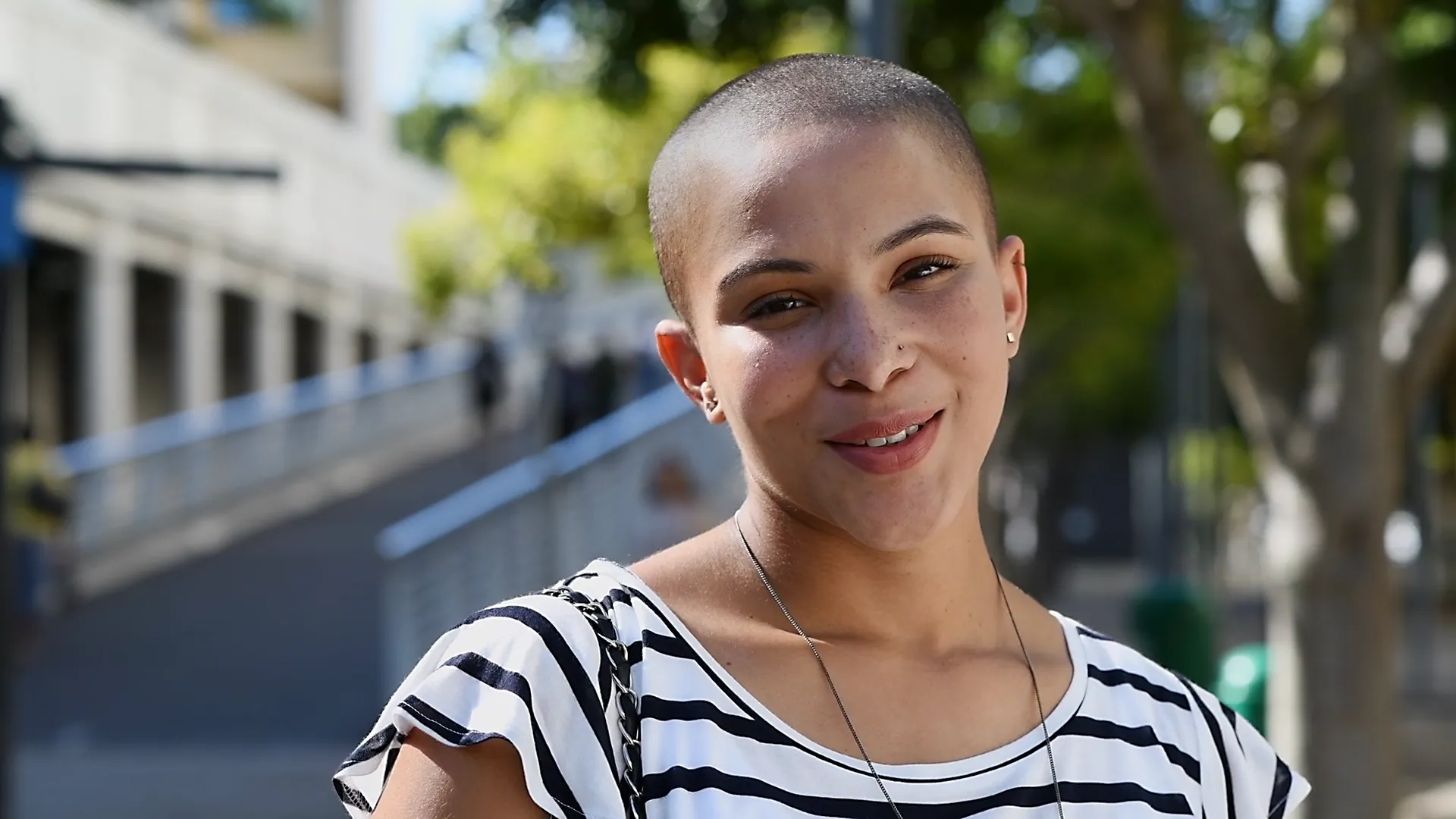 Junge Frau mit rasiertem Kopf lächelt in die Kamera und trägt ein gestreiftes Shirt – authentisches Porträt mit positiver Ausstrahlung.