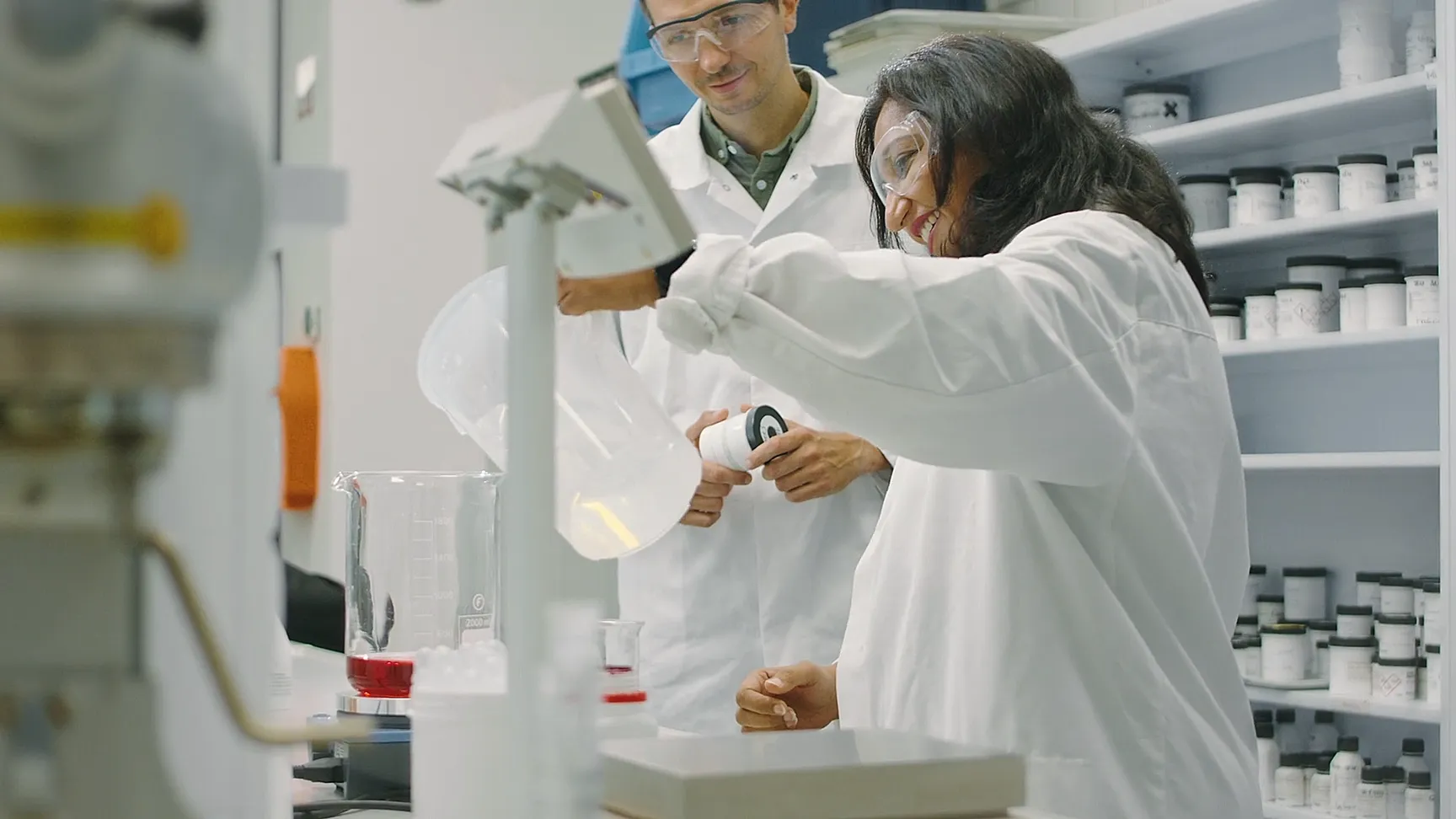 Hände in Laborkitteln gießen rote Flüssigkeiten in kleine Gläser für Tests im Givaudan-Labor.