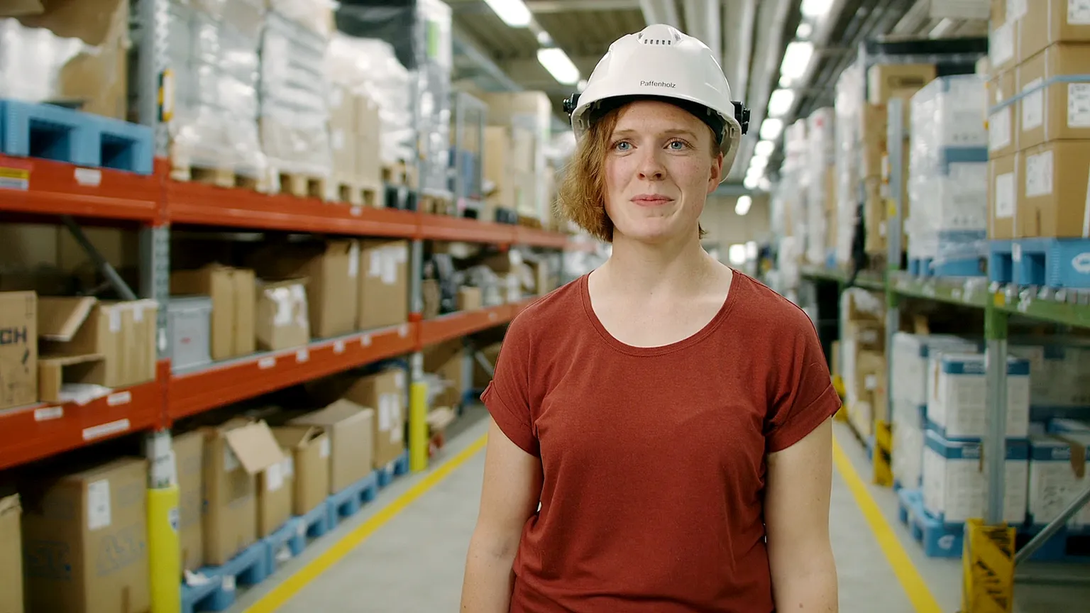Mitarbeiterin bei Givaudan mit Helm im Lagerbereich zwischen hohen Regalen mit Kartons.