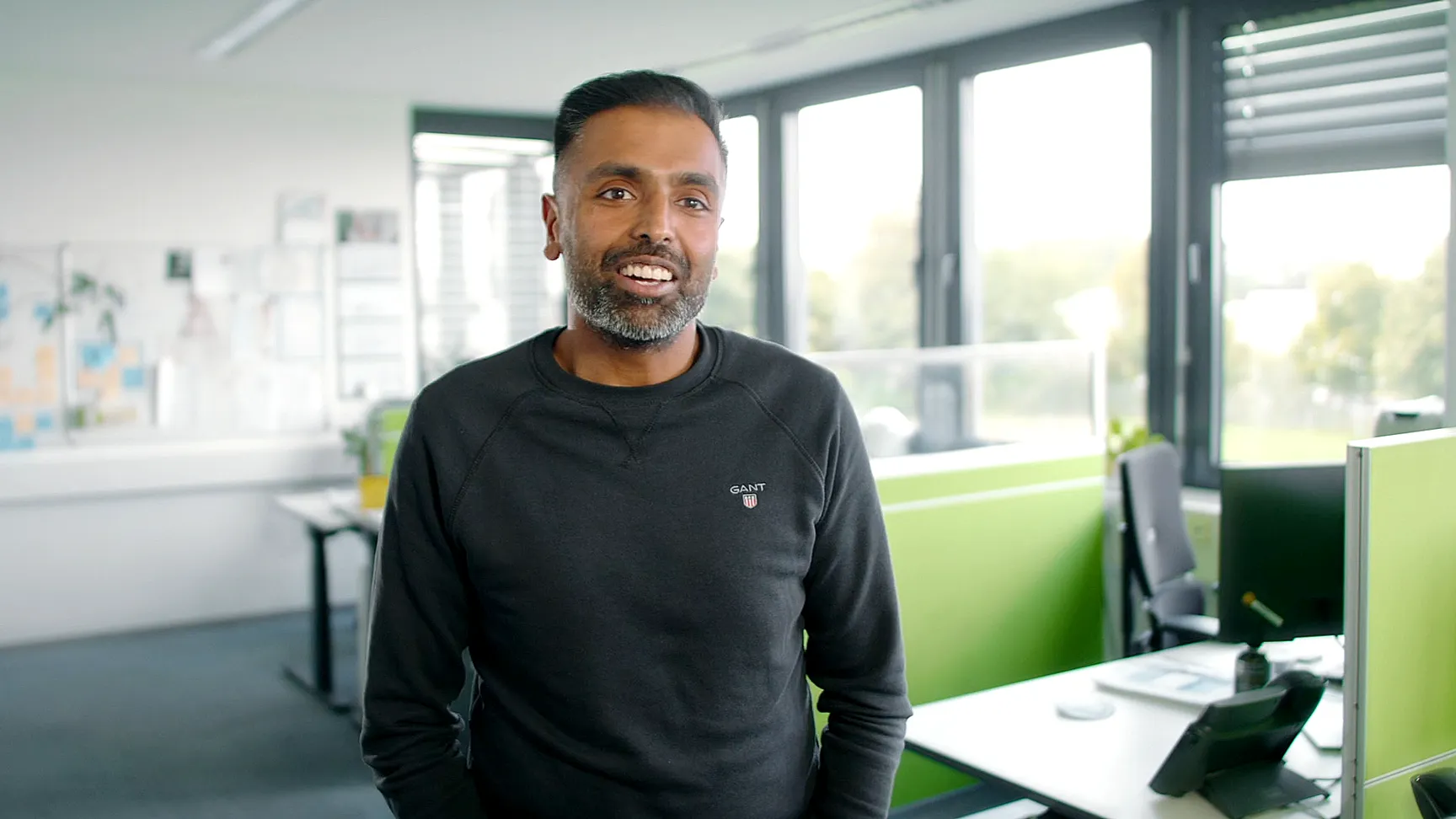 Mitarbeiter im Büro von Givaudan, lächelt in die Kamera, im Hintergrund moderne Arbeitsplätze.