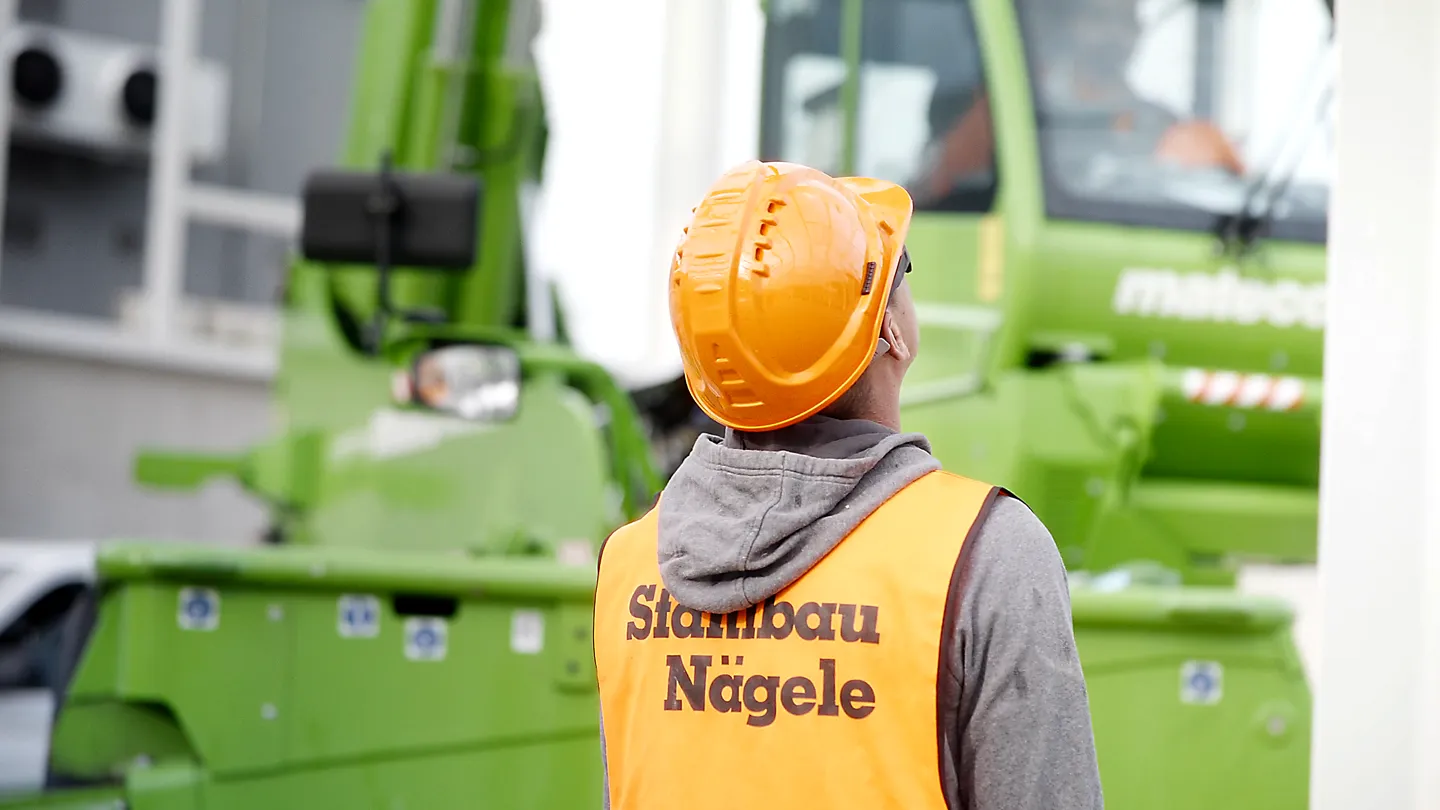 Filmproduktion Szene: Bauarbeiter von Stahlbau Nägele mit Sicherheitshelm und Warnweste vor grünem Kran – authentische Industrieaufnahme für Imagefilm, Unternehmensfilm und Filmproduktion im Stahl- und Bauwesen.