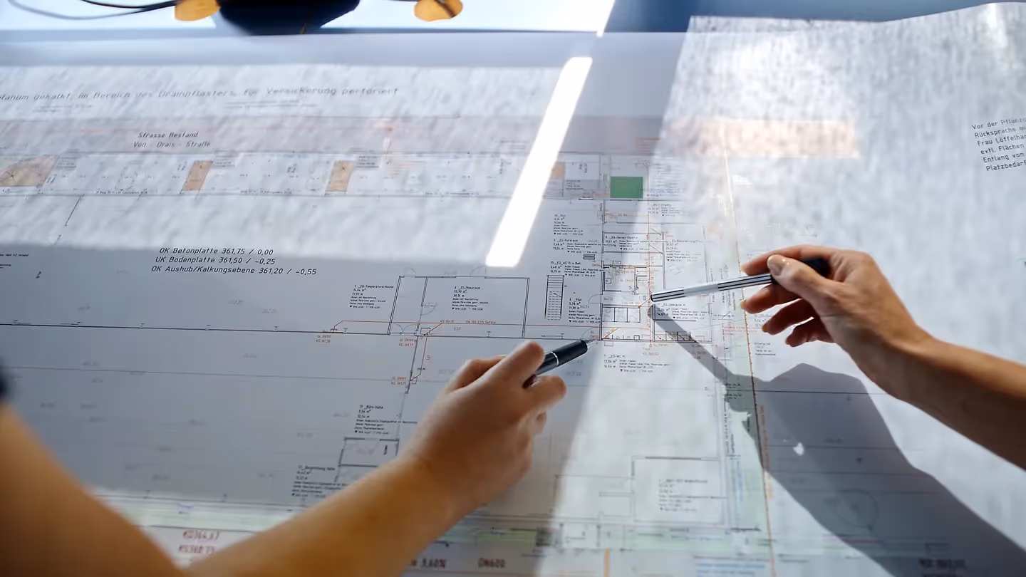 Filmproduktion Szene: Detailaufnahme von zwei Händen, die auf technische Baupläne zeigen – Industrieaufnahme für Unternehmensfilm, Imagefilm und Filmproduktion im Ingenieurwesen und technischen Projektmanagement.