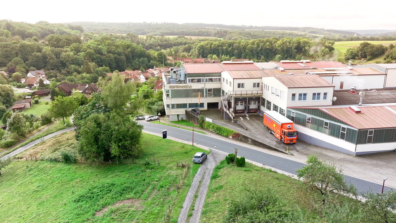 Rüdinger Spedition Lkw vor Firmengebäude in ländlicher Umgebung, Drohnenaufnahme mit Lagerhalle und Natur.
