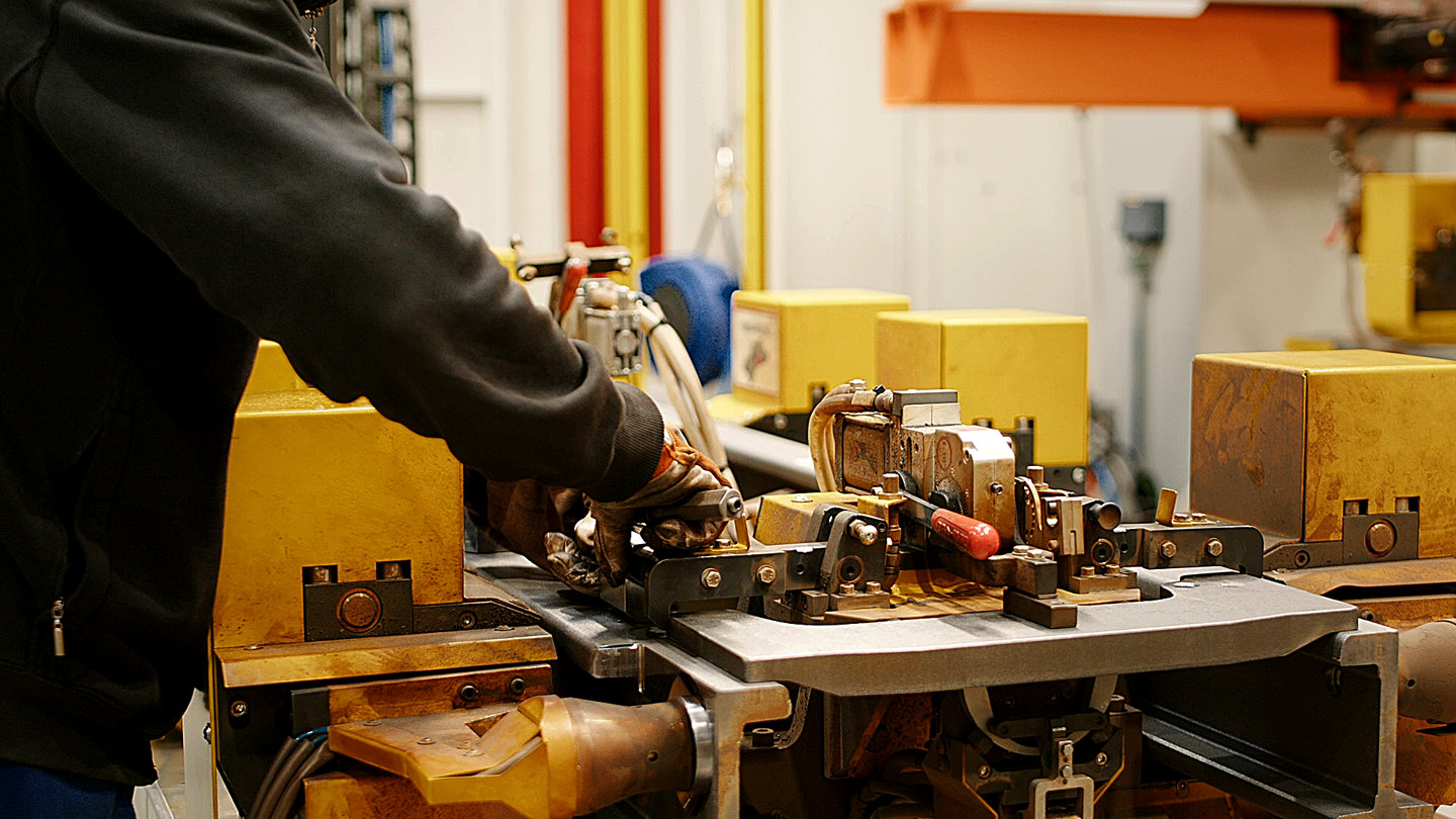 Mitarbeiter bedient eine industrielle Metallpresse in der KION Produktion, präzise Fertigung von Bauteilen mit gelben Maschinenmodulen in moderner Werkhalle.