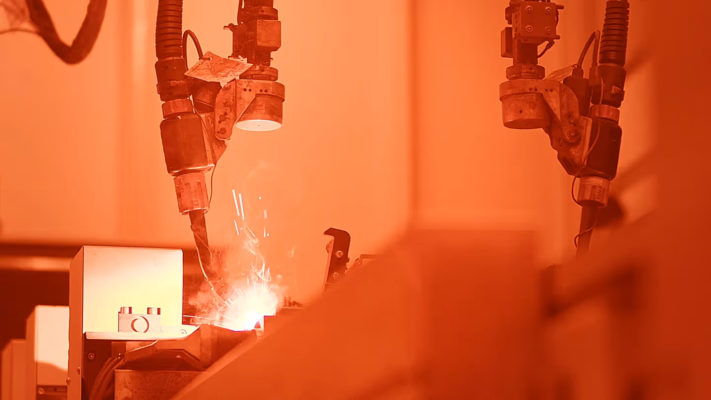 Industrieroboter beim Schweißen in der KION Produktion, Nahaufnahme der Schweißroboter durch Schutzglas mit sichtbaren Funken und Lichtbogen.