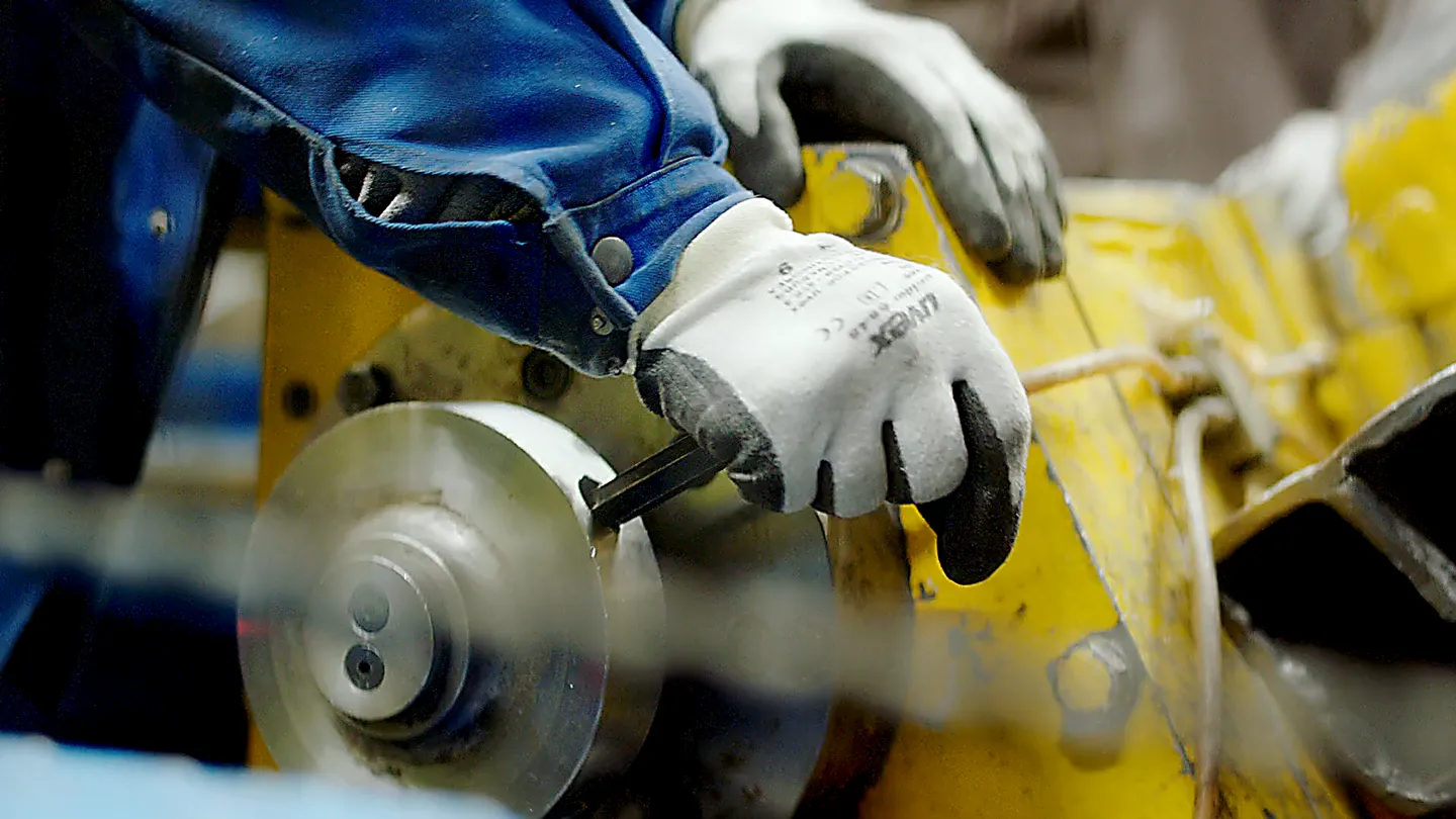 Nahaufnahme eines Arbeiters in Handschuhen, der eine Industriemaschine justiert, präzise Metallbearbeitung in moderner Produktion.