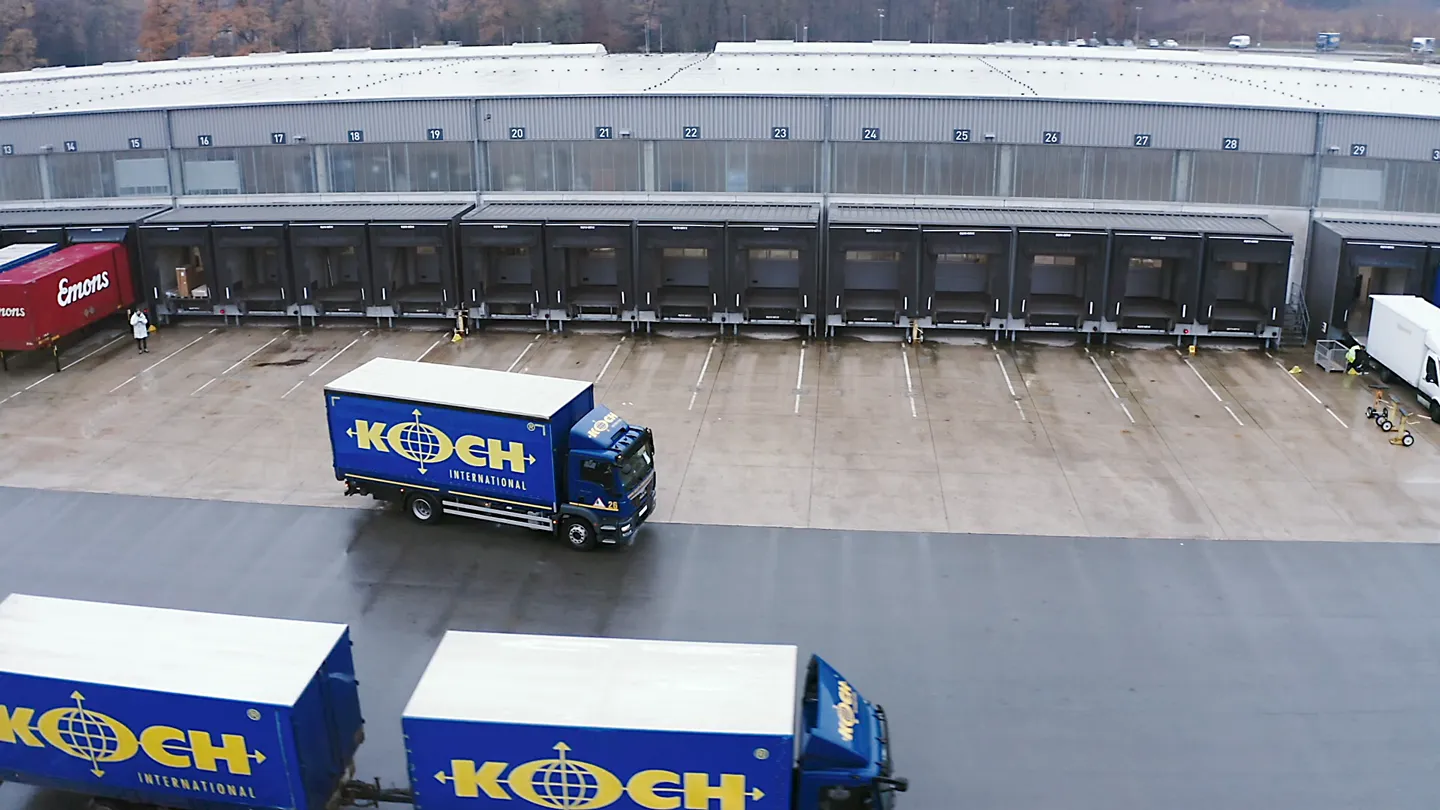 Luftaufnahme eines Logistikzentrums mit Ladebuchten, Koch International LKWs und weiteren Transportfahrzeugen.