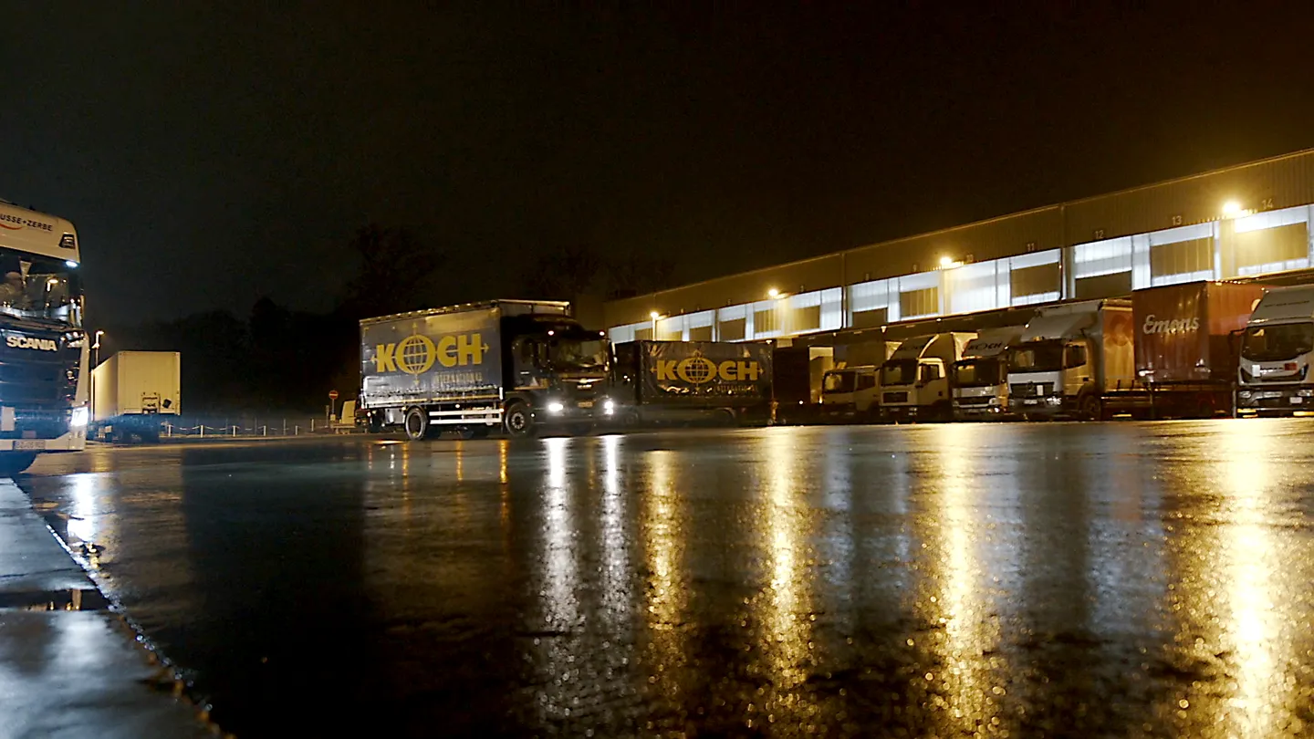 Speditionshof bei Nacht mit beleuchteten LKWs und Ladezonen, Koch Logistik LKW im Vordergrund.