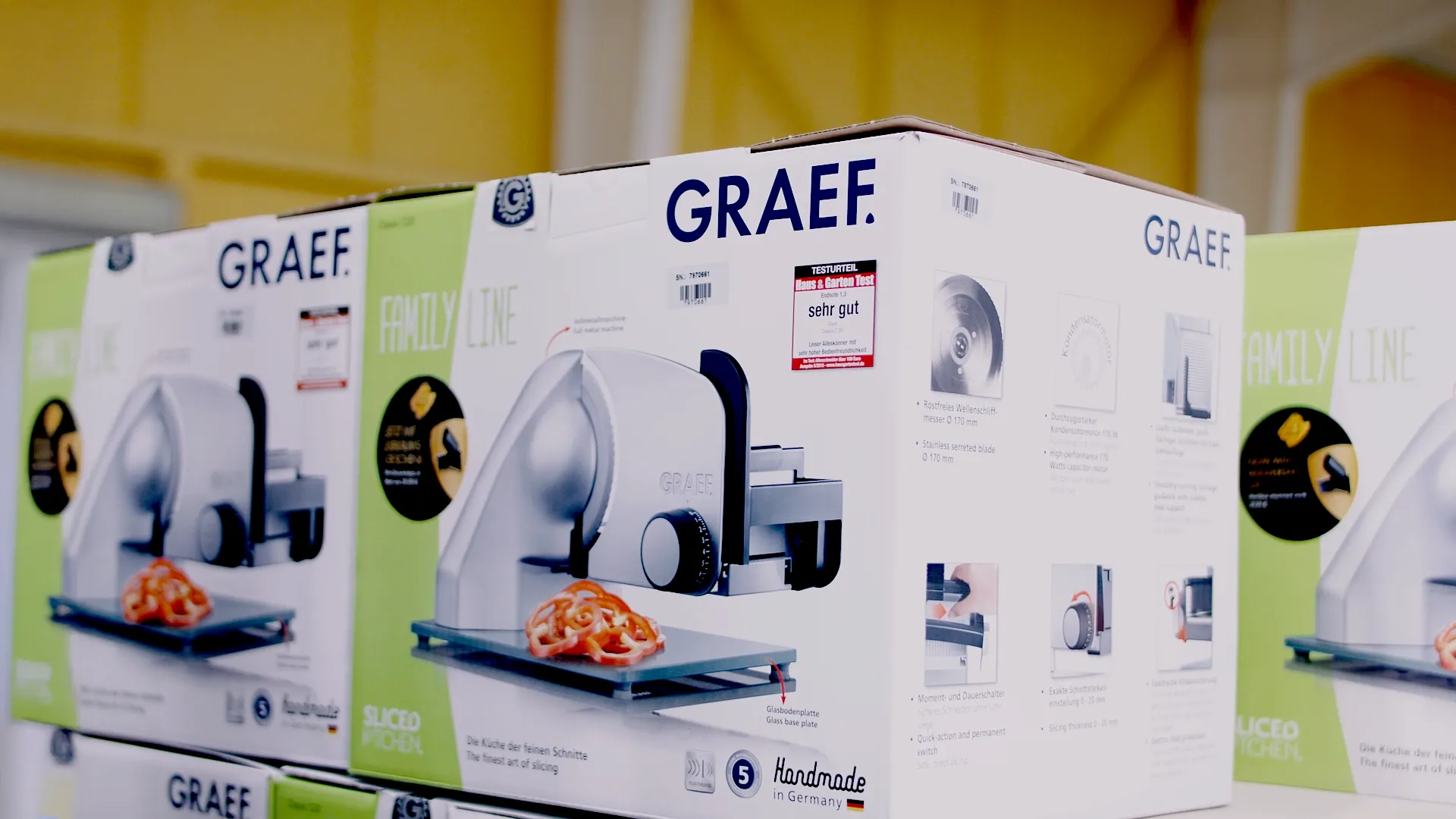 Gestapelte Verpackungen der Graef Family Line Allesschneider, mit Produktabbildung und Testurteil „sehr gut“ auf der Vorderseite, aufgenommen in einer Produktions- oder Lagerumgebung.