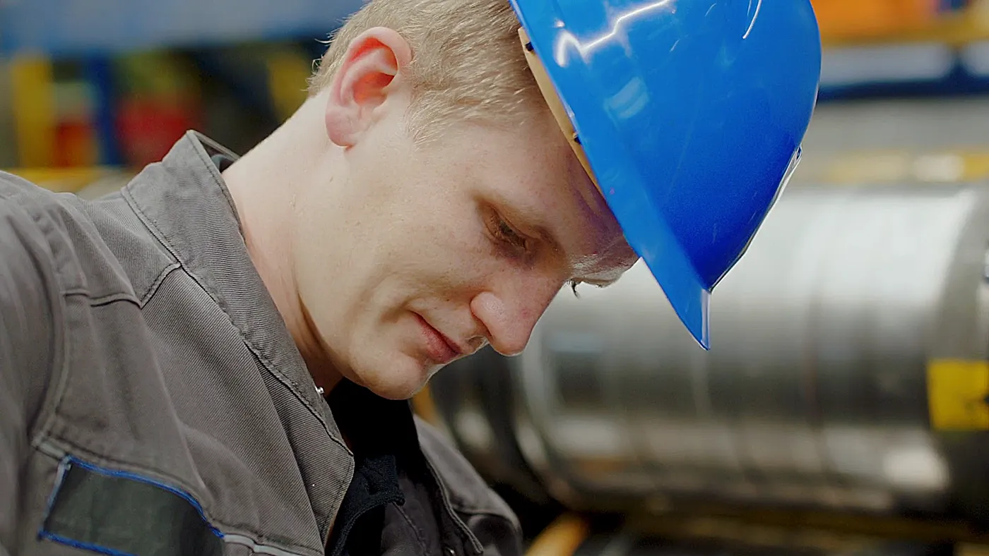 Junger Mitarbeiter mit blauem Schutzhelm arbeitet konzentriert in der Produktion – industrielle Fertigung und Nachwuchs im Handwerk.